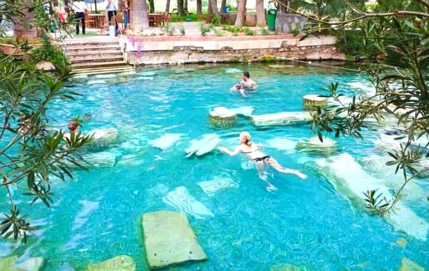 Personas nadando entre ruinas sumergidas en una piscina de agua cristalina rodeada de vegetación