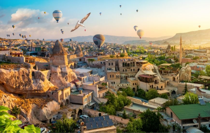 Globos aerostáticos sobrevuelan el pueblo de Göreme con formaciones rocosas y construcciones típicas al atardecer.
