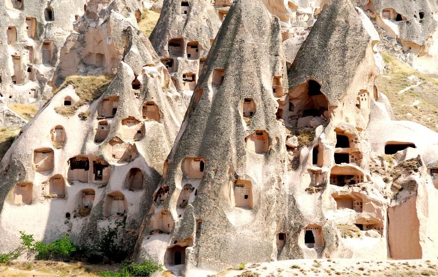 Casas talladas en formaciones rocosas cónicas típicas de Capadocia con múltiples ventanas y entradas.