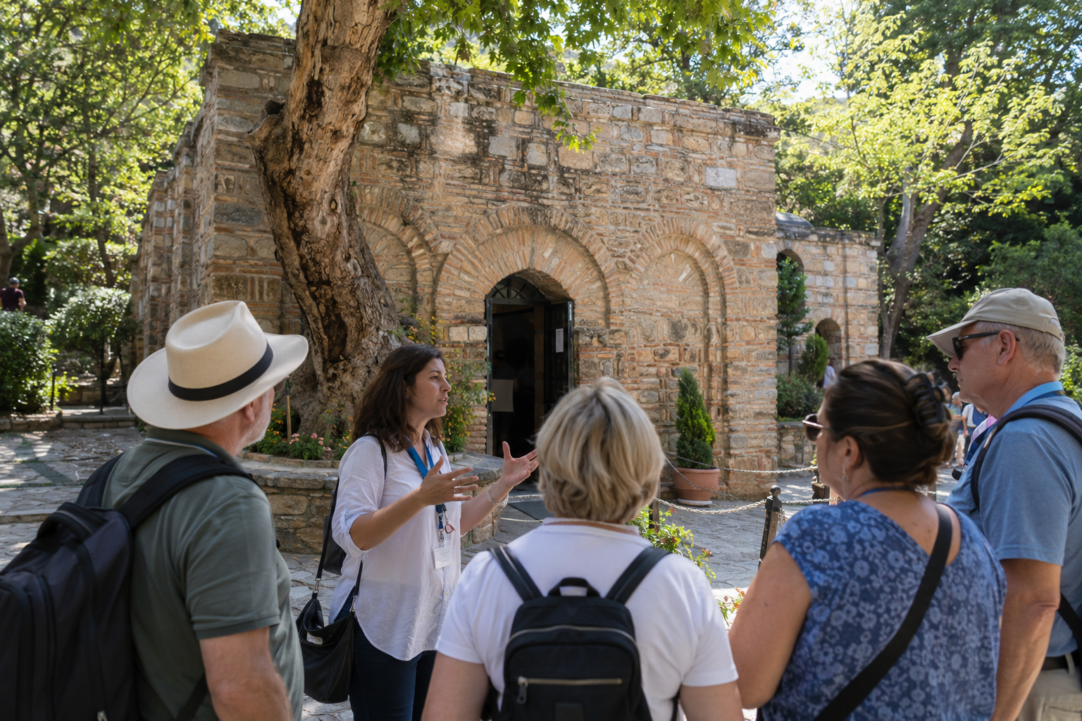 Guía turística explicando la historia frente a la Casa de la Virgen María, en un entorno tranquilo con árboles y senderos de piedra.