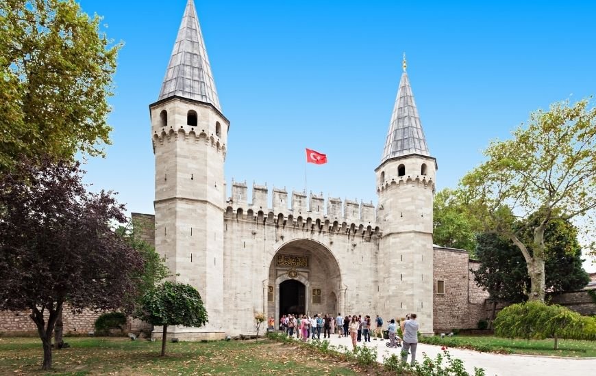 Entrada principal del Palacio de Topkapi con visitantes y bandera turca ondeando al viento