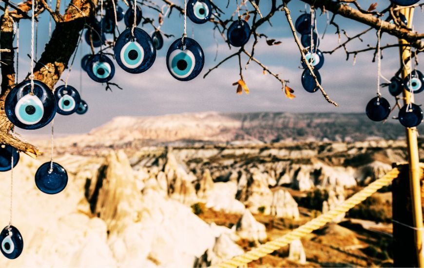 Amuletos de ojo turco colgados en ramas con las chimeneas de hadas de Capadocia al fondo