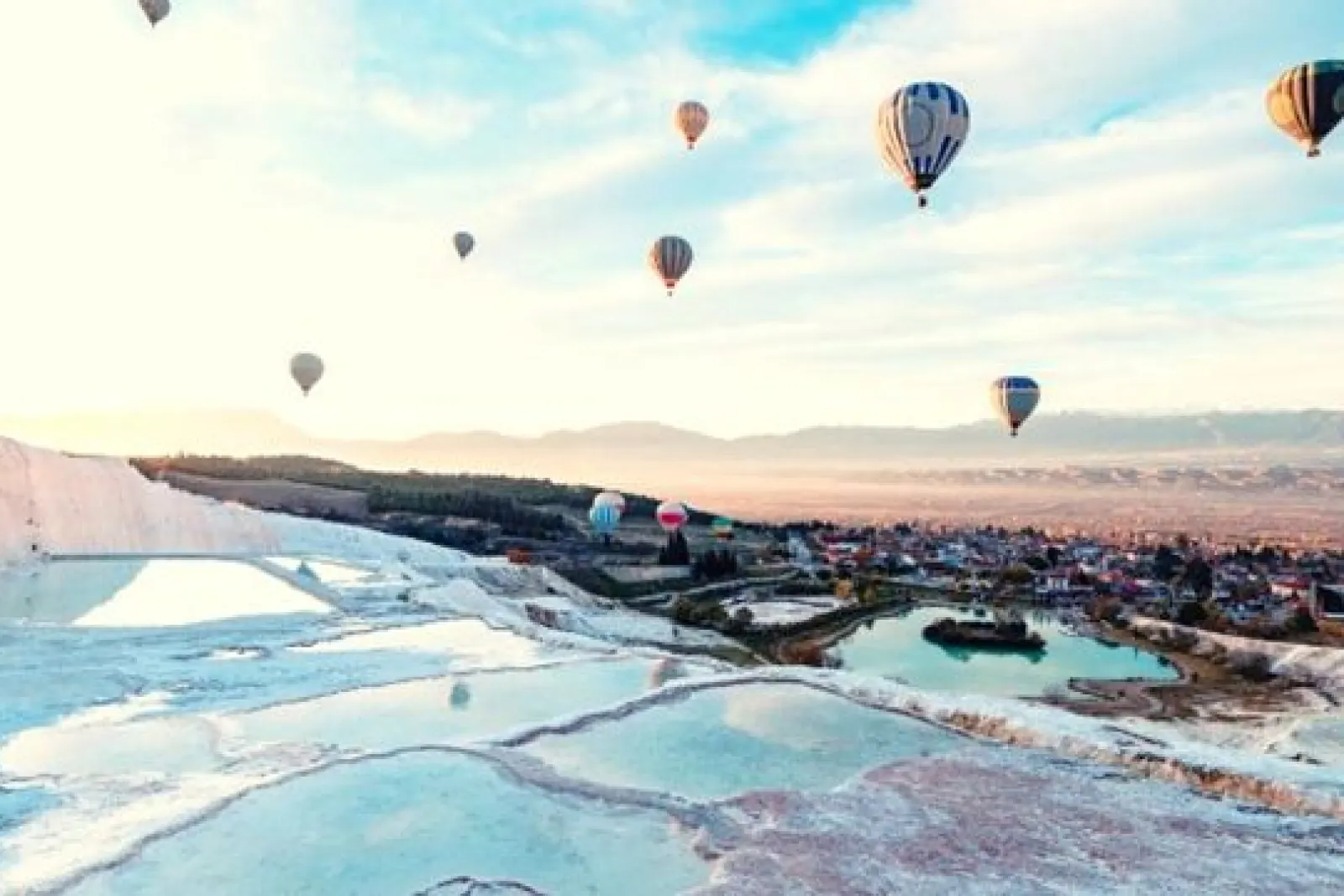 Globos aerostáticos sobre las terrazas blancas de travertinos con piscinas en Pamukkale al amanecer.