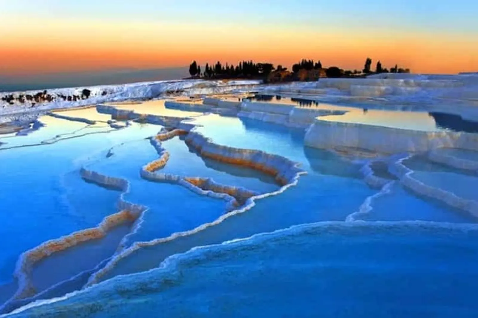 Piscinas termales escalonadas de travertino con agua azul bajo un cielo al atardecer en Pamukkale.