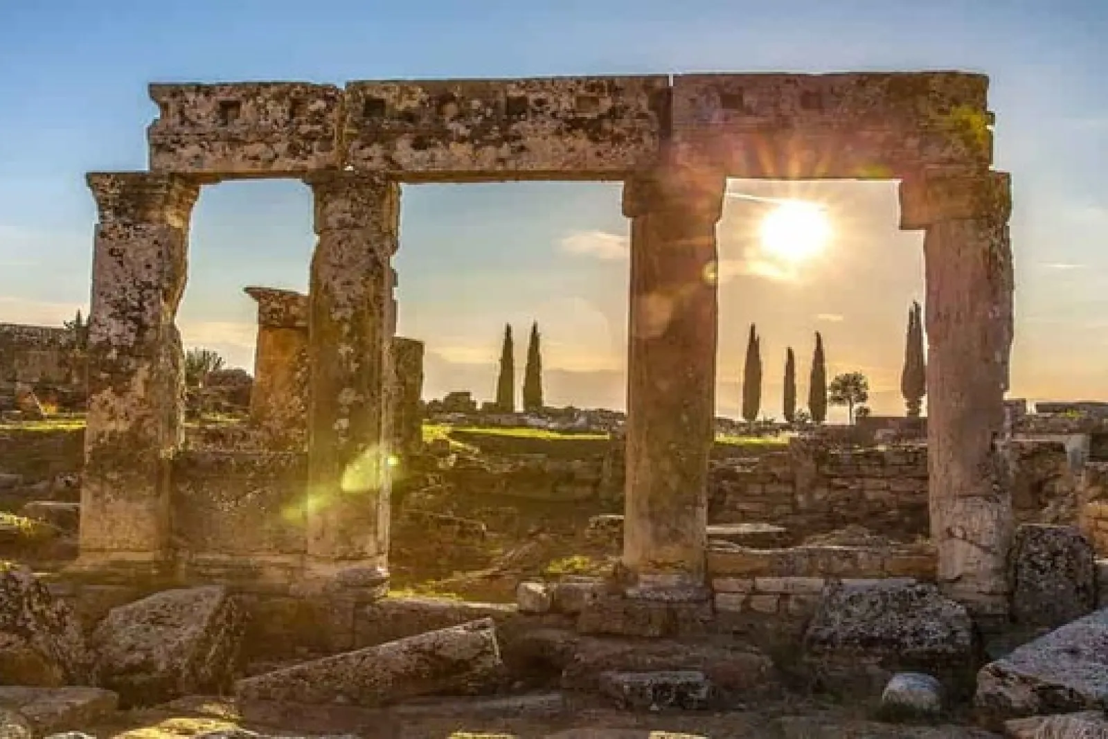 Ruinas antiguas con columnas y arco bajo el sol al atardecer en un sitio arqueológico abierto