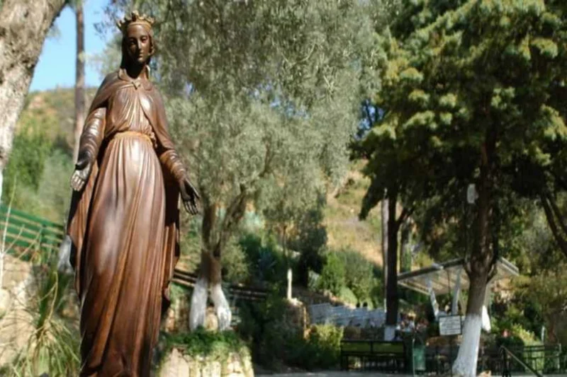 Estatua de la Virgen María en el complejo de la Casa de la Virgen María, rodeada de árboles, jardines y senderos de piedra.