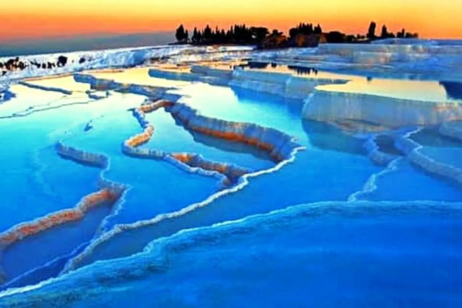 Piscinas termales de travertino en Pamukkale con agua azul reflejando la luz del atardecer en la cima de la colina.
