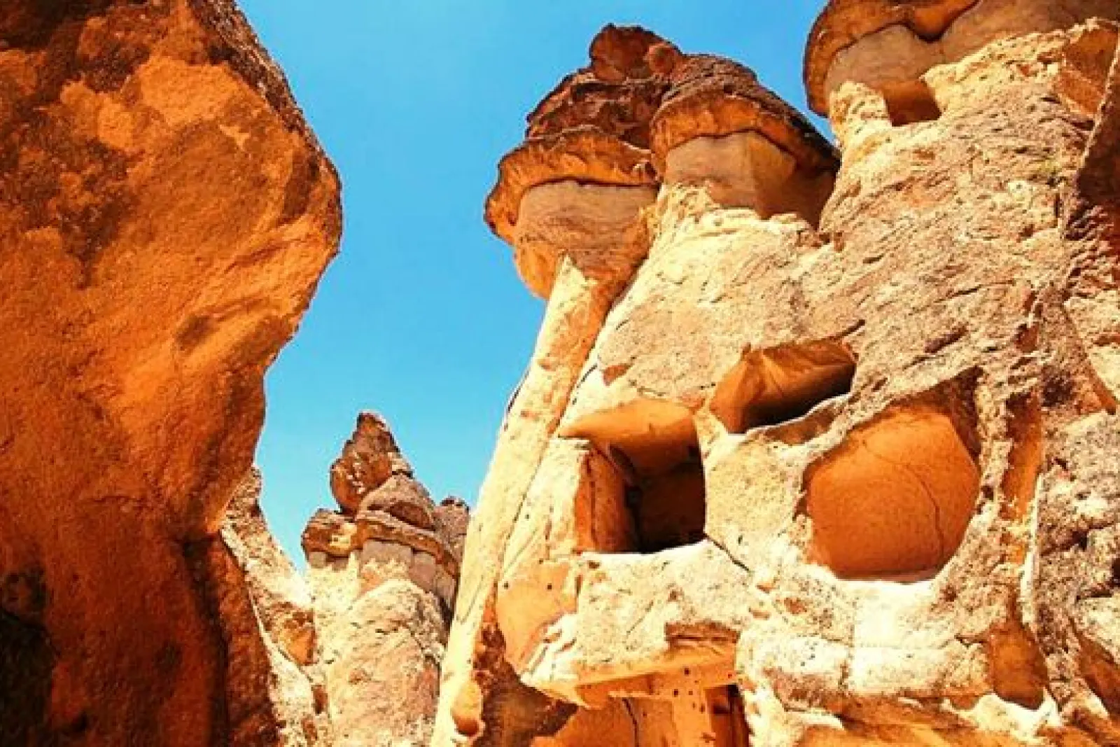 Formaciones rocosas de Capadocia con cuevas talladas en la piedra bajo un cielo azul claro en paisaje árido.