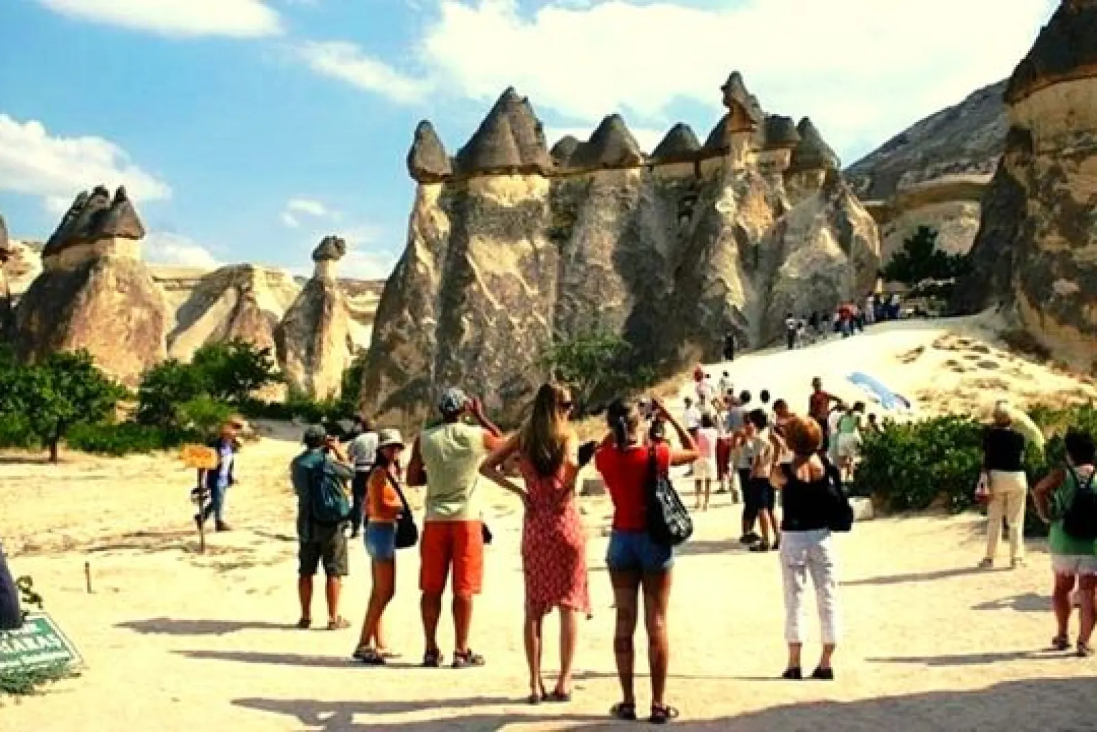 Turistas fotografiando las chimeneas de hadas en un valle rocoso de Capadocia bajo el cielo azul.