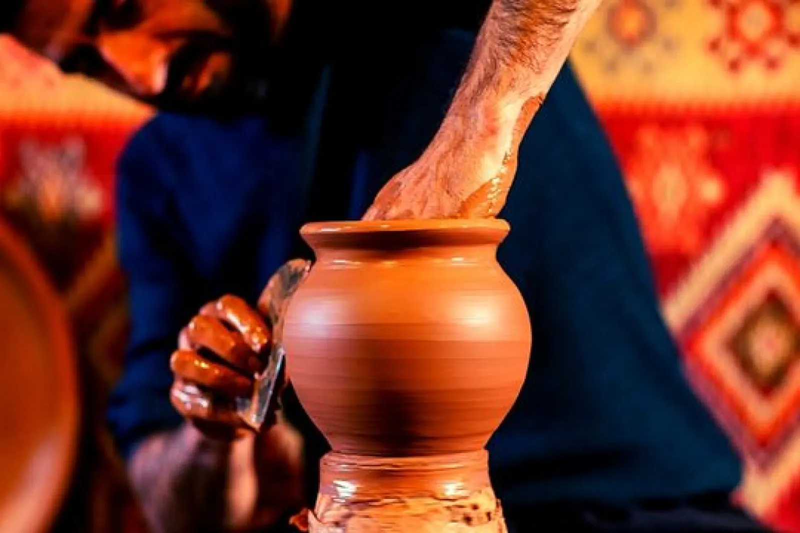 Alfarero moldeando una vasija de barro en un taller de cerámica tradicional de Avanos, con tapices coloridos al fondo.
