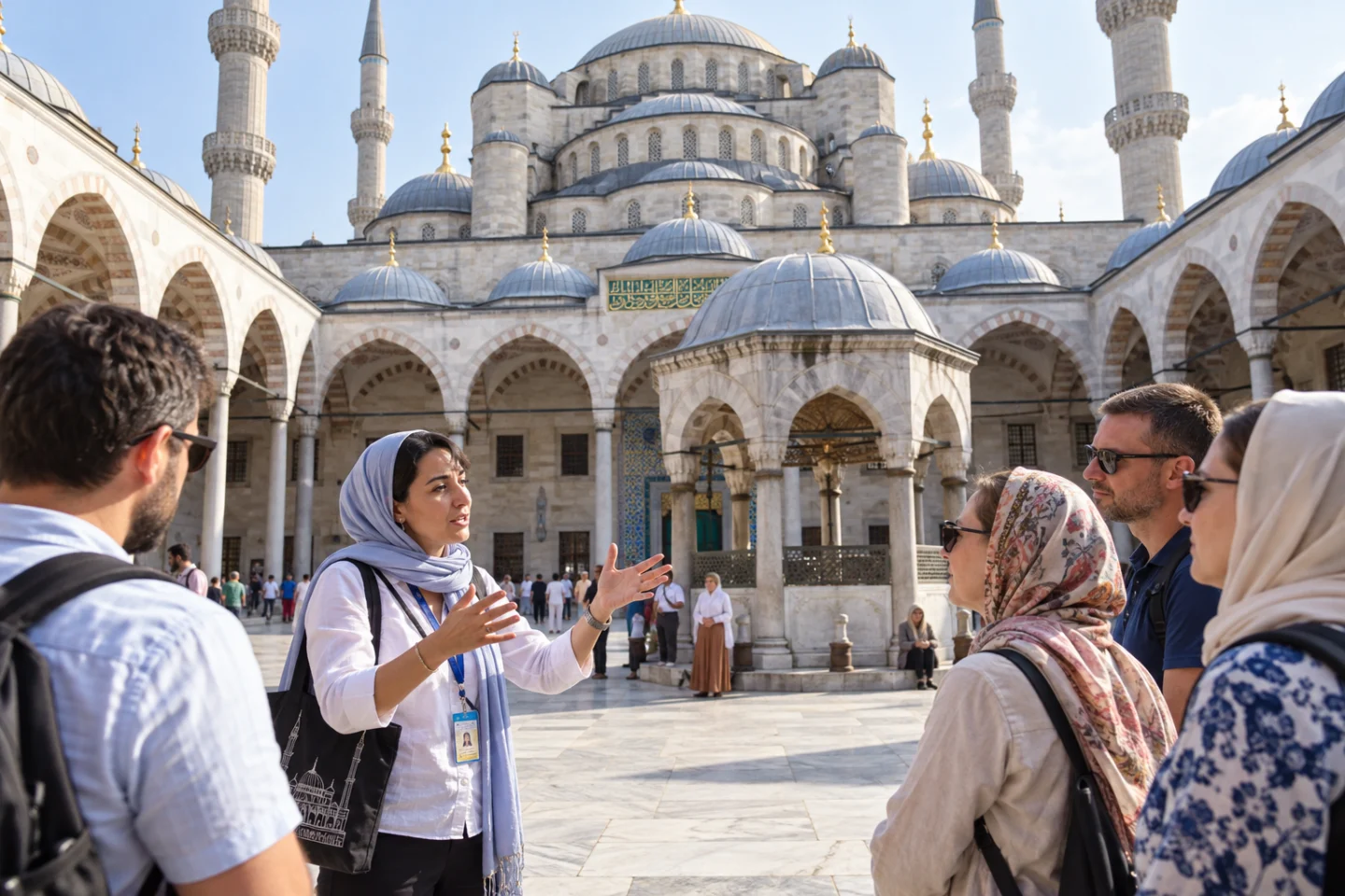 Grupo de turistas escuchando a una guía en el patio interior de la Mezquita Azul de Estambul, con cúpulas y minaretes al fondo.